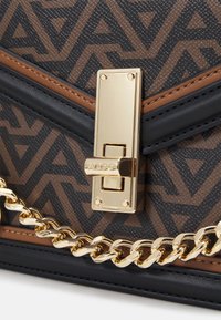 Borsa a tracolla geometrica con motivo in tessuto marrone e nero, dotata di una chiusura dorata e una tracolla a catena. Presenta dettagli in pelle liscia e elementi di design audaci.