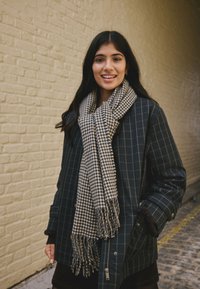 Dark navy plaid coat with a button-up front, paired with a checkered scarf. The scarf features fringed edges and a textured fabric.