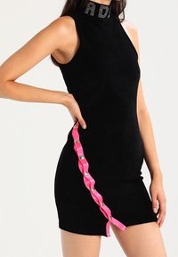 Svart ärmlös klänning med hög halsringning, som har en rosa banddetalj med silverknappar på sidan och en figursydd siluett.