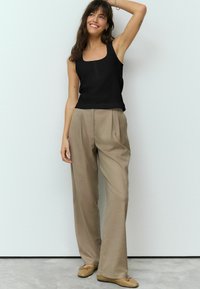 Top nero in tessuto strutturato con scollatura quadrata e dettagli con bottoni, abbinato a pantaloni beige a vita alta con pieghe e ballerine beige.