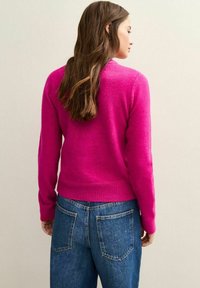 Fuksjowy sweter z prążkowanym wykończeniem u dołu i na mankietach, wykonany z miękkiego materiału. W zestawie ze średnio wypłukanymi, luźnymi dżinsami.