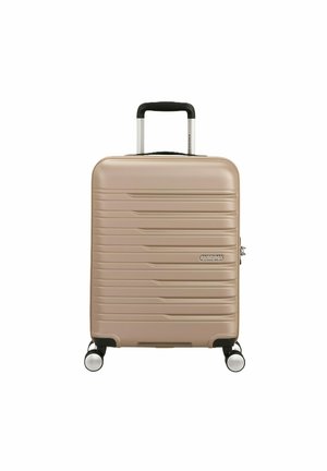 Maleta rígida beige con ranuras horizontales, cuatro ruedas giratorias y mango telescópico extendido hacia arriba.