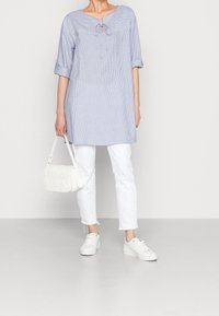 Tunic a righe azzurro chiaro con scollatura rotonda e dettaglio con fiocco. Abbinato a jeans bianchi usurati e sneakers bianche. Porta una borsa bianca trapuntata.