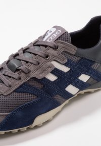 Chaussure de sport grise et marine en mesh et daim, avec des accents blancs, des lacets ronds et une semelle en caoutchouc texturée.