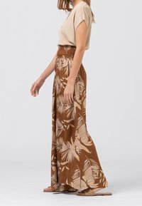 Hnědá květinová maxi sukně s nabraným pasem, kombinovaná s béžovým krátkým rukávem s rib chabou. Viditelný vzor listů palmy.