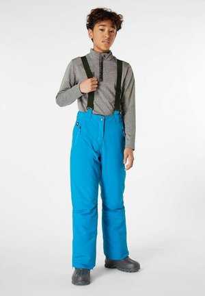 Blauwe waterdichte skibroek met verstelbare groene bretels, heeft zijzakken en een relaxte pasvorm; gedragen over een grijze lange mouwen top.