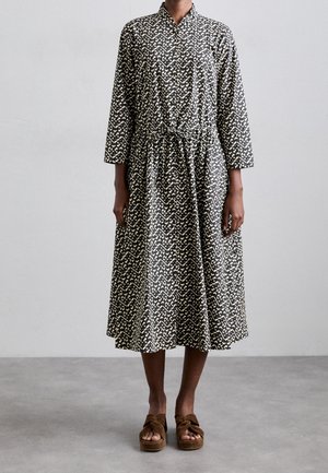 Czarna i biała sukienka midi w wzory z długimi rękawami i paskiem w talii, noszona z brązowymi, otwartymi sandałami na platformie.