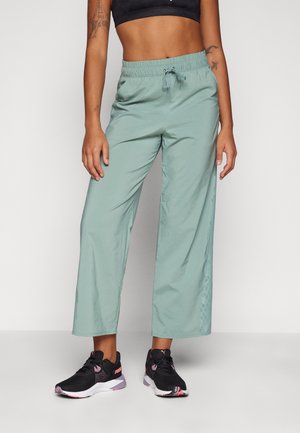 Pantalons larges vert clair avec une taille élastique et un cordon de serrage ; présente des accents de panneaux en maille sur les côtés. Portés avec des chaussures de sport noires.