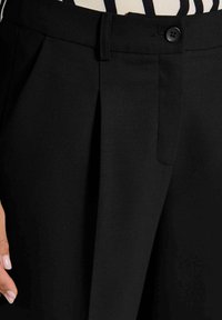 Schwarze, taillierte Hose mit Faltendesign, Knopfverschluss und glattem, strukturiertem Stoff. Es sind keine sichtbaren Taschen zu sehen.