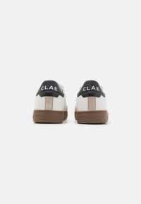 Hvite lær sneakers med en svart hæltab med "CLAE"-branding, brune suedetaljer og en brun gummisåle.
