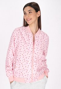 Roze bomberjack met rode kersenprint, geribbelde manchetten en tailleband. Voorzien van een rits aan de voorkant en twee zijzakken. Glad stof textuur.