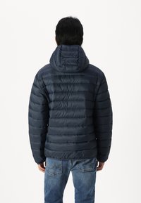 Marineblå pufferjakke med horisontale quiltede paneler, hette og elastiske mansjetter, kombinert med lyseblå jeans.