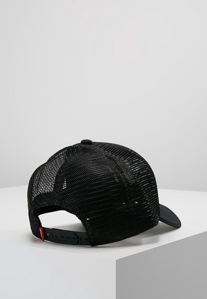 Czarna siatkowa czapka z daszkiem na zatrzask z regulowanym paskiem, spoczywająca na białej powierzchni na tle jednolitego szarego tła.