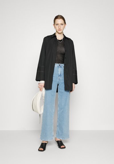 Black oversized button-up shirt over a sheer top, paired with high-waisted light blue wide-leg jeans and black slide sandals. White handbag.