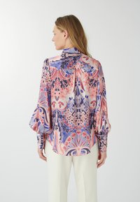 Garā piedurkņu blūze izgatavota no zīda maisījuma, ar krāsainu ziedu un paisley rakstu rozā, violetā un zilā krāsā. Maigs savelkums pie pleciem.