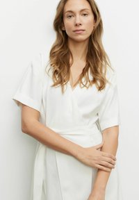 Biała sukienka w stylu wrap z krótkimi rękawami, dekoltem w serek, paskiem w talii oraz gładkiego, lekkiego materiału. Minimalistyczny design bez wzorów czy ozdób.