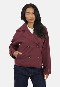 Veste double boutonnage bordeaux avec de grands boutons marron, un large col et des sangles de poignet ajustables. Tissu léger, coupe décontractée, poches latérales.