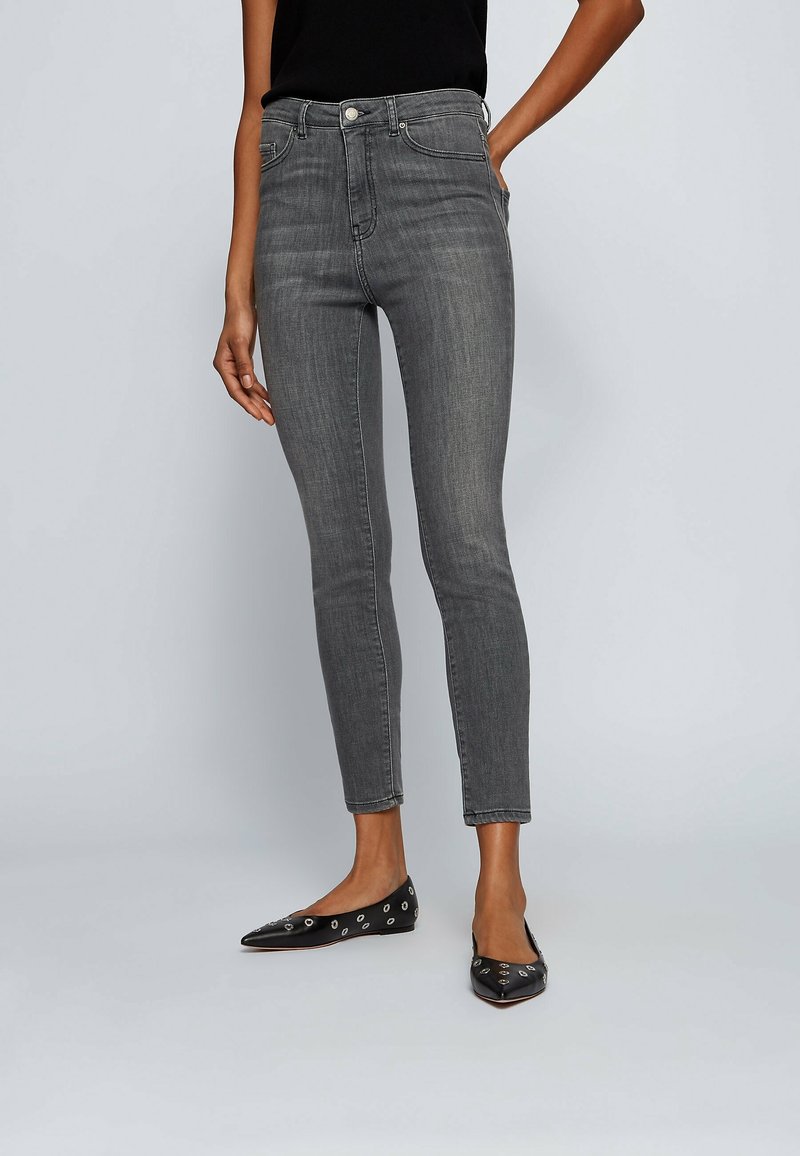 Jean skinny gris en denim avec une taille haute, une coupe slim, un design à cinq poches et un ourlet brut ; associé à des ballerines noires pointues.