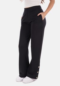 Pantaloni neri a gamba larga con vita elasticizzata, tasche laterali e bottoni decorativi in tono dorato sull'orlo inferiore. Tessuto dalla texture morbida.