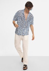 Korte mouwen, blauw patroon overhemd met een kraag, gecombineerd met lichtbeige linnen broek en zwarte sandalen, wat een ontspannen pasvorm laat zien.