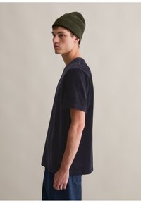 Granatowa bawełniana koszulka z krótkim rękawem, luźny krój, okrągły dekolt i miękka tekstura. W zestawieniu z ciemnozielonym prążkowym czapką.