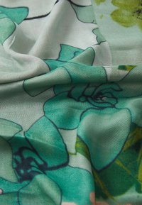 Tessuto morbido con uno sfondo verde chiaro caratterizzato da grandi motivi floreali sovrapposti in verdi più scuri e sottili accenti di giallo.