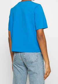 Camiseta de algodón azul con un corte relajado, mangas cortas y cuello redondo. Presenta una textura suave y un detalle de costura mínimo. Llevada con jeans de mezclilla claros.