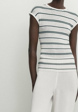 Person wearing a fitted white ribbed shirt with black horizontal stripes and loose white pants against a plain light background.