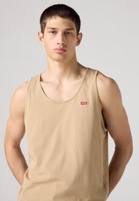 Bež majica bez rukava od pamuka, s okruglim izrezom i malim crvenim Levi's logotipom. Glatka tekstura s prilagođenim dizajnom.