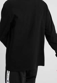 Sort langærmet t-shirt lavet af bomuld med en afslappet pasform. Den har en rund halsudskæring og let sænkede skuldre, med en glat tekstur.