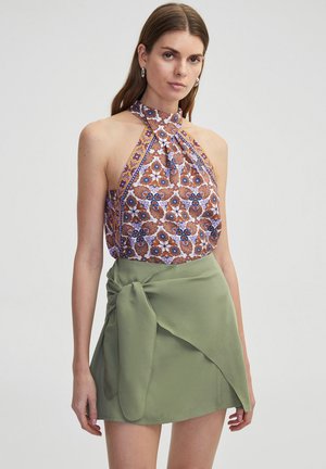 Halterneck top met bloemenpatroon in bruin en blauw, gecombineerd met een groene wikkel mini-jurk met een strikdetail op de taille.