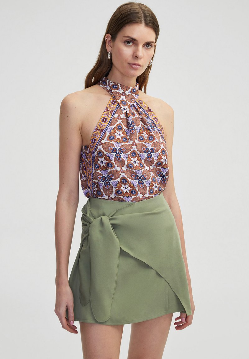 Halterneck top met bloemenpatroon in bruin en blauw, gecombineerd met een groene wikkel mini-jurk met een strikdetail op de taille.