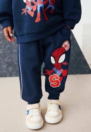 Felpa blu navy e pantaloni abbinati con grafiche colorate di Spider-Man. Tessuto morbido con strisce bianche sui lati e sneakers beige.