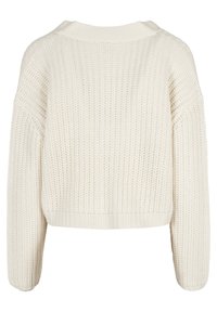 Krämfärgad tjockstickad tröja med långa ärmar och ribbad nederkant, sedd bakifrån.