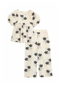 Ensemble pour enfants en deux pièces comprenant un haut crème avec des manches bouffantes et un imprimé floral noir, associé à un pantalon assorti avec imprimé noir.
