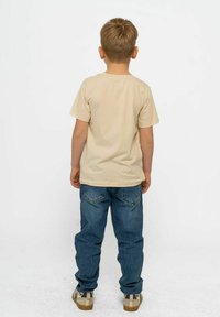 Beige T-Shirt mit kurzen Ärmeln und Rundhalsausschnitt, kombiniert mit blauen Jeans. Das Outfit zeichnet sich durch einen lässigen Schnitt und ein schlichtes Design aus.