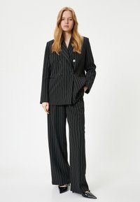 Blazer noir à rayures, double boutonnage et revers pointus, associé à un pantalon à jambes larges. Comprend de grands boutons et une texture de tissu lisse.