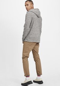 Gray textured hoodie with a hood, paired with rolled-cuff tan pants and light shoes featuring black soles and white socks with red stripes.