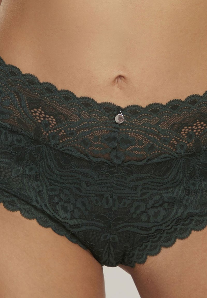 Donkergroene kanten bikini slip met geschulpte randen en intrigerende bloemenpatronen, voorzien van een kleine metalen accent in het midden voor.