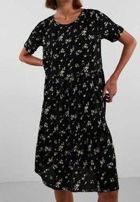 Černé květinové šaty s krátkými rukávy, kulatým výstřihem a nařasenou sukní. Obsahují malý bílý květinový vzor a lehkou texturu materiálu.