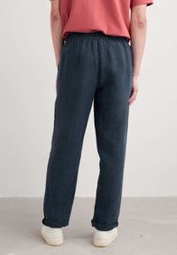 Linen blend, loose-fitting dark gray pants with an elastic waistband, rolled cuffs, and a textured surface. Worn with a short-sleeve top.