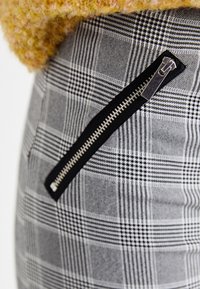 Close-up van een zilveren rits op een zwart-wit geruit stof met een textuur van een mosterdgele gebreide kleding erboven.