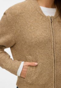 Beidzolēts vilnas maisījuma jaku ar rāvējslēdzēju, ribotiem piedurknēm un sānu kabatām. Tekstūrēta virsma un apaļas kakla dizains.