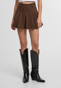 Hnědá skladaná sukně s pevným pasem. Spárována s černými vysokými botami po kolena s špičatou špičkou a zakřiveným horním okrajem.