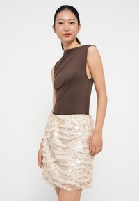 Bodysuit sans manches marron associé à une jupe en sequins beige ajustée ornée de motifs ondulés et d'accents scintillants, créant une apparence texturée.