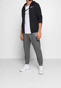 Nike träningskläder bestående av en svart zip-up hoodie, en vit t-shirt med kort ärm och logotyp, samt grå joggingbyxor. Avslutat med vita sneakers.