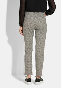 Strakke, gemusterde broek met een geometrisch ontwerp in neutrale tinten, met een gladde textuur en een enkel-lange snit, gecombineerd met zwarte sneakers.