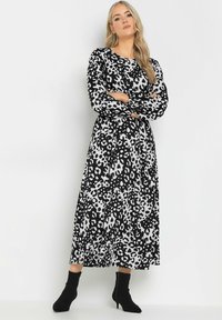 Langärmliges Kleid mit Schwarz-Weiß-Leopardenmuster, Rundhalsausschnitt und fließender Silhouette, kombiniert mit schwarzen Knöchelstiefeln.