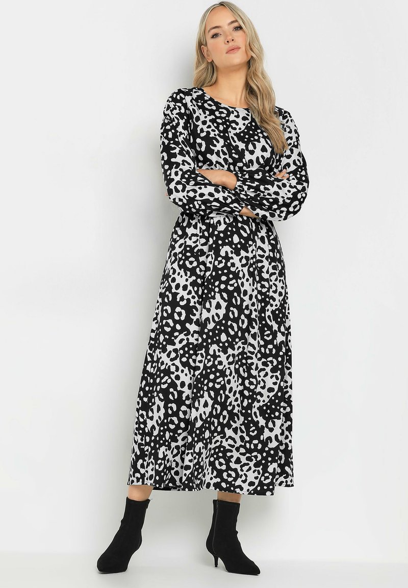 Langärmliges Kleid mit Schwarz-Weiß-Leopardenmuster, Rundhalsausschnitt und fließender Silhouette, kombiniert mit schwarzen Knöchelstiefeln.