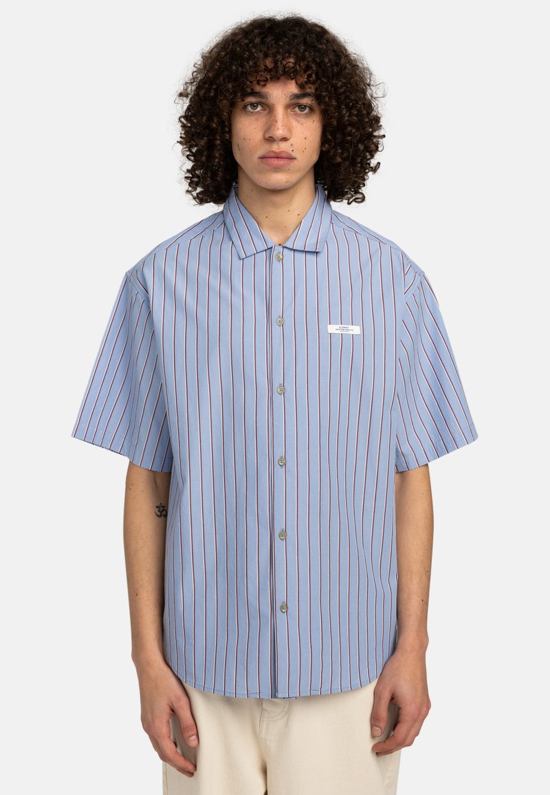 Camicia a maniche corte con bottoni in tessuto azzurro chiaro, con righe verticali rosse e bianche, dotata di colletto a punta e di una piccola etichetta con logo.